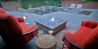 A fire pit sitting on a patio next to red chairs.