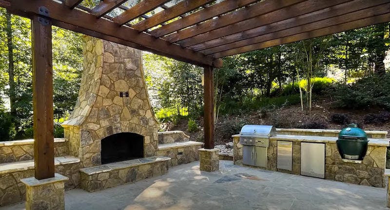 Outdoor kitchen with a stone fireplace and grill.