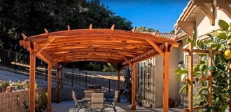 A patio covered in a wooden pergola next to home.