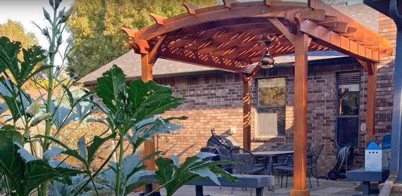 Patio covered in a wooden pergola next to a brick building.